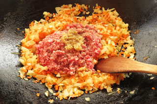 野菜を炒めているフライパンにひき肉とおろし生姜を入れる。