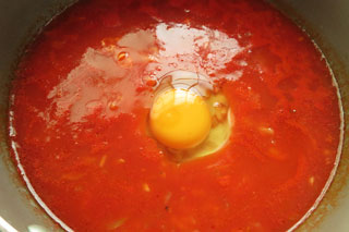 トマト雑炊を煮込んでいる鍋に卵をおとす。