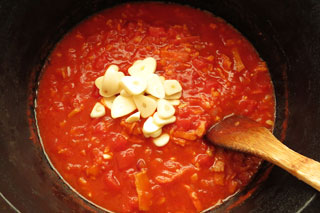 煮込んでいるにんにくのトマトソースに、にんにくのうす切りを入れる。