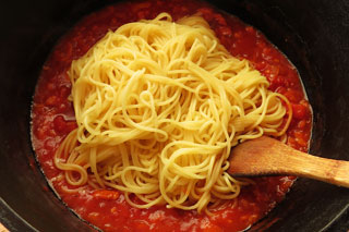にんにくのトマトソースを煮込んでいる鍋に、ゆでたスパゲティを入れる。