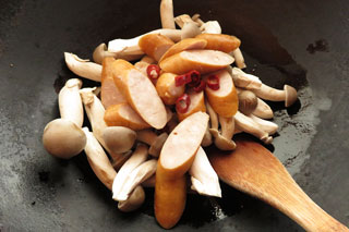 にんにくを炒めているフライパンに、ハタケシメジとウインナーソーセージ、鷹の爪、酒大さじ1を入れる。