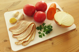分量の目安。まな板に置いたトマトと玉ねぎ、にんじん、にんにく、生姜、ベーコン。