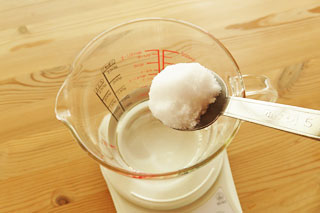 計量カップに入った水に塩をくわえる。