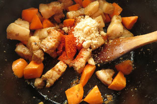 豚肉を炒めている鍋ににんじんと砂糖、一味唐辛子を入れる。
