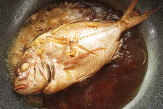 煮汁を煮詰めている鯛の煮付け。