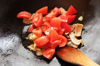 にんにくとベーコンを炒めているフライパンに生トマトを入れる。