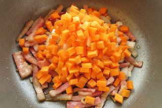 ベーコンとにんにく、鷹の爪を炒めている鍋に、玉ねぎとにんじんを入れる。